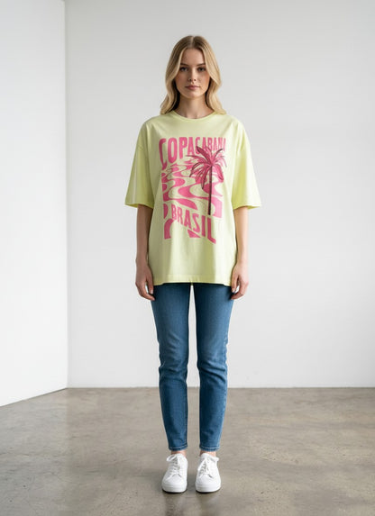 Modelo veste camiseta Aoi Closet Farm Rio amarela neon oversized com estampa rosa Copacabana Brasil em algodão.